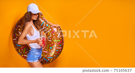 Young woman girl posing with donut-shaped swim inflatable ring isolated on yellow background. Young woman girl posing with donut-shaped swim inflatable ring isolated on yellow background. 75105637