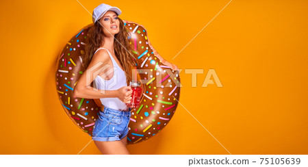 Young woman girl posing with donut-shaped swim inflatable ring isolated on yellow background. Young woman girl posing with donut-shaped swim inflatable ring isolated on yellow background. 75105639
