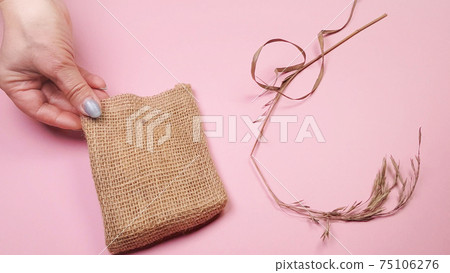 Florist hands prepare dry grass and canvas bag for composition, on pink background, DIY concept Florist hands prepare dry grass and canvas bag for composition, on pink background, DIY concept 75106276
