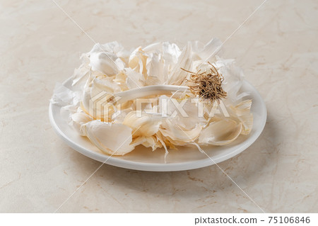 Dry husk of white garlic on a small plate over a kitchen table. Dry husk of white garlic on a small plate over a kitchen table. 75106846
