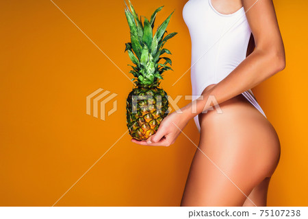 Female buttocks, sexy ass. Young sporty woman holding a pineappl 75107238