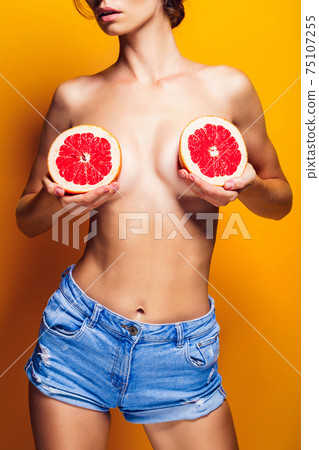 Crop woman holding grapefruit near breasts 75107255