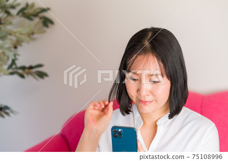 A woman fixing her hair with a smartphone camera 75108996