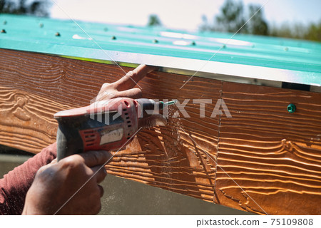 Unsafe Male Roofer Workman Using Electric Screwdriver Install Tile on Roof of New House in the Construction Site with no Protection 75109808