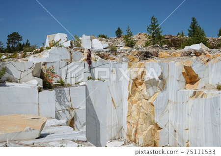 Girl sits on the edge of huge marble quarry Girl sits on the edge of huge marble quarry 75111533