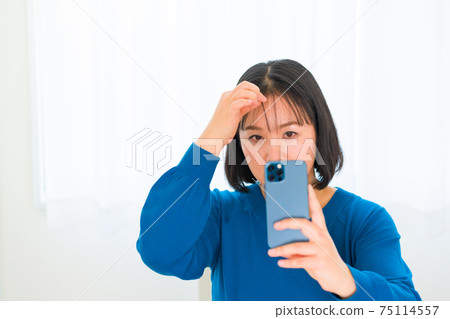 A woman fixing her hair with a smartphone camera 75114557