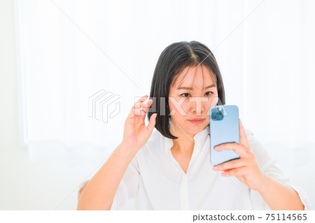 A woman fixing her hair with a smartphone camera 75114565