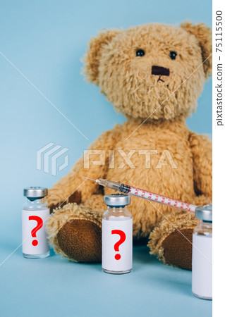 Vertical image of teddy bear with unnamed vial dose of vaccine or another medicine with syringe against blue background with copy space - vaccine hesitancy or anti-vax concept. Selective focus Vertical image of teddy bear with unnamed vial dose of vaccine or another medicine with syringe against blue background with copy space - vaccine hesitancy or anti-vax concept. Selective focus 75115500