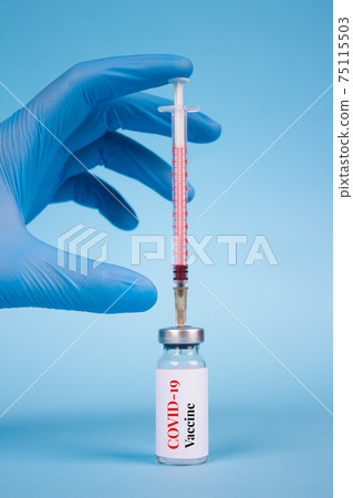 Vertical image of doctor or scientist holding vial dose of COVID-19 vaccine with syringe against blue background with copy space - prevention coronavirus, global vaccination concept. Selective focus Vertical image of doctor or scientist holding vial dose of COVID-19 vaccine with syringe against blue background with copy space - prevention coronavirus, global vaccination concept. Selective focus 75115503