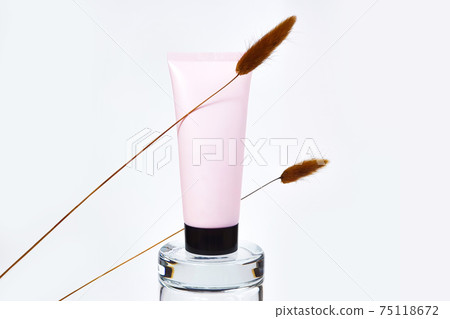 Pink squeeze bottle cream tube with black cap and brown herbs Lagurus. Cosmetic bottle for branding and label on glass podium on white background. Mockup style, minimalism. 75118672