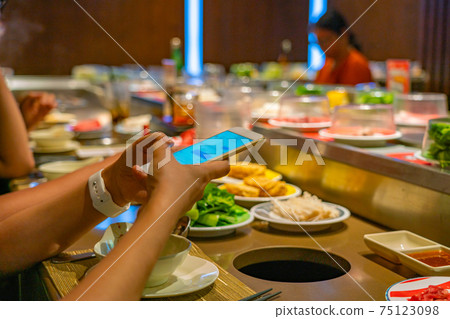Young people using smartphone while eating at conveyor belt hotpot restaurant 75123098