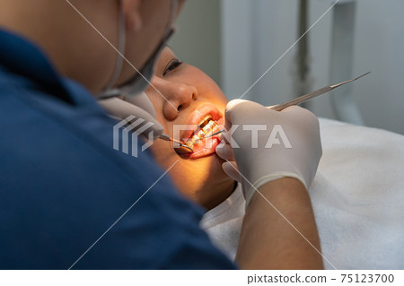 Rear view photo of woman having dental treatment at clinic  75123700