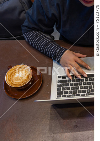 Close up photo of female's hand using laptop and having latte coffee Close up photo of female's hand using laptop and having latte coffee 75123779