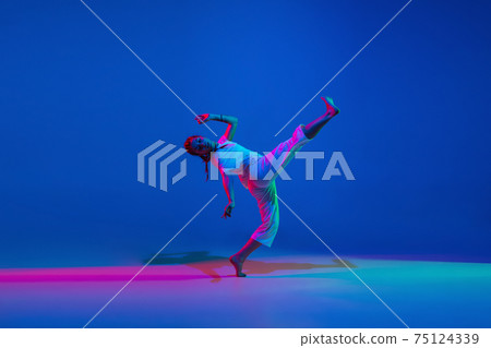 Beautiful girl dancing hip-hop in white attire on blue background in neon light 75124339