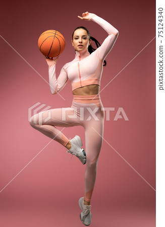 Beautiful young woman with basketball ball jumping in the air 75124340