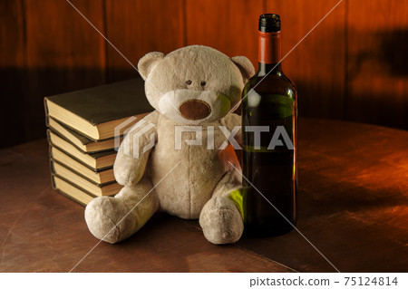 Alcohol and children abuse. Teddy bear as a symbol of child's safety and bottle on a table Alcohol and children abuse. Teddy bear as a symbol of child's safety and bottle on a table 75124814