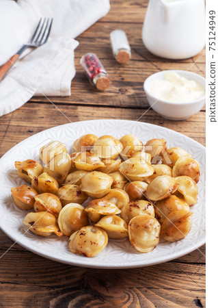 Traditional fried pelmeni, ravioli, dumplings filled with meat on plate, russian kitchen. Wooden rustic table, copy space. Traditional fried pelmeni, ravioli, dumplings filled with meat on plate, russian kitchen. Wooden rustic table, copy space. 75124949