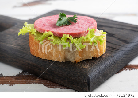 Sandwiches with lettuce leaves and sliced salami sausage on a wooden Board. Sandwiches with lettuce leaves and sliced salami sausage on a wooden Board. 75124972
