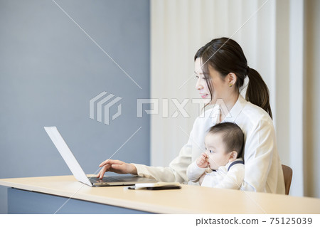 A woman holding a baby and operating a laptop A woman holding a baby and operating a laptop 75125039