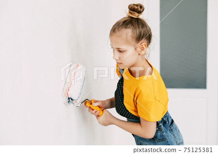 A girl in a denim overalls and a yellow T-shirt helps to paint the walls in an apartment white 75125381