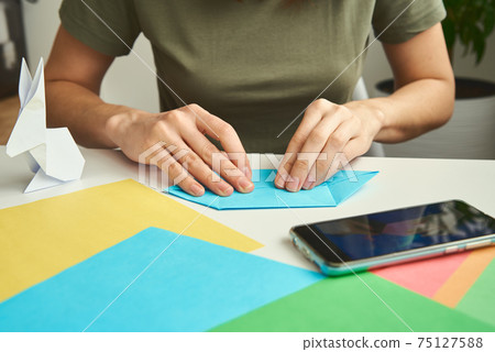 DIY concept. Woman make origami easter rabbit from color paper. Origami lessons DIY concept. Woman make origami easter rabbit from color paper. Origami lessons 75127588