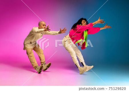 Stylish sportive caucasian couple dancing hip-hop on colorful gradient background at dance hall in neon light. 75129820
