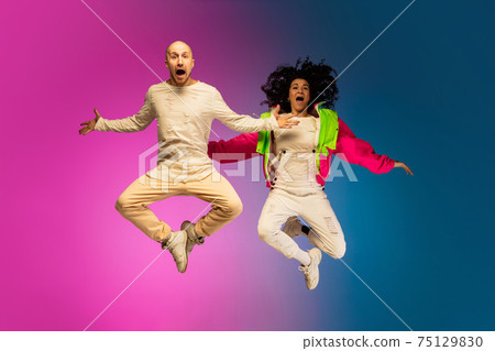 Stylish sportive caucasian couple dancing hip-hop on colorful gradient background at dance hall in neon light. 75129830