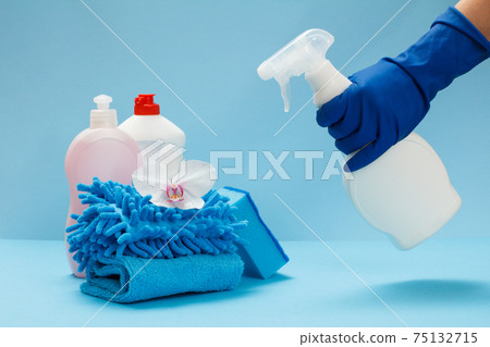 Woman's hand in a protective glove with a bottle of glass and tile cleaner on the blue background. Woman's hand in a protective glove with a bottle of glass and tile cleaner on the blue background. 75132715