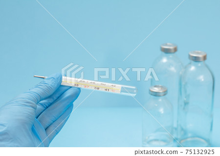 Doctor in latex gloves holding a glass mercury thermometer on blue background. Doctor in latex gloves holding a glass mercury thermometer on blue background. 75132925