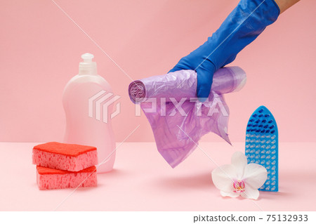 Bottle of dishwashing liquid, sponges and hand with garbage bags on pink background. 75132933