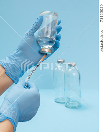 Doctor's hands in latex gloves holding syringe and picking up liquid medicine for injection. Doctor's hands in latex gloves holding syringe and picking up liquid medicine for injection. 75133039