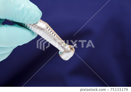 Dentist's hand in green examination glove with dental handpiece. Dentist's hand in green examination glove with dental handpiece. 75133179