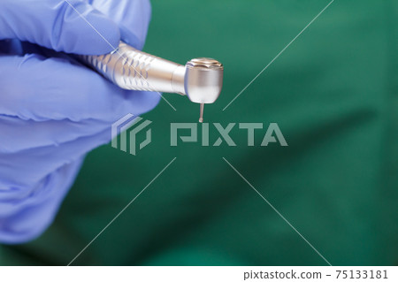 Dentist's hand in glove with dental handpiece. 75133181