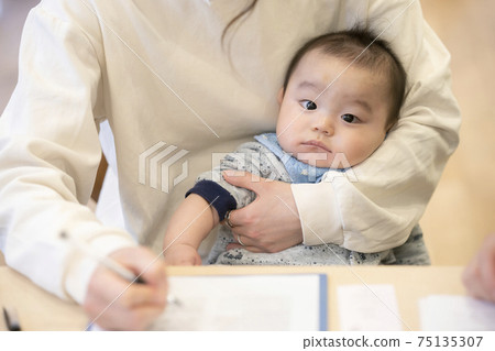 Baby held by a mother doing desk work 75135307