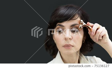 Woman smoothes folds and wrinkles on the skin with a facial massager 75136127