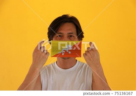 A man with Bhutan flag on hygienic mask in his hand and lifted up the front face A man with Bhutan flag on hygienic mask in his hand and lifted up the front face 75136167