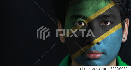 Portrait of a man with the flag of the Tanzania painted on his face on black background 75136681