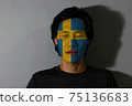 Portrait of a man with Sweden flag painted on his face and close eyes with black shadow 75136683