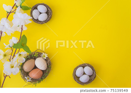 Happy easter holiday greeting card. Birdnests with eggs and branch of blooming cherry on yellow background. Space for text, top view Happy easter holiday greeting card. Birdnests with eggs and branch of blooming cherry on yellow background. Space for text, top view 75139549