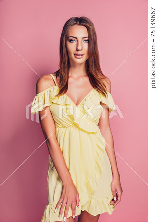 Pretty young woman in yellow dress posing on pink background Pretty young woman in yellow dress posing on pink background 75139667