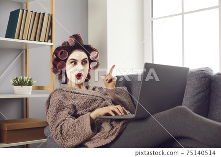 Woman in curlers and face mask browsing Internet and learning amazing life hacks and ideas 75140514
