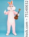 Happy funny musician kid boy or girl guitarist is playing music by ukulele or Hawaiian guitar. Easter bunny or rabbit or hare celebrates Happy easter, plays music by instrument 75140632