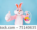 Happy easter. Easter bunny or rabbit or hare holds egg with basket of colored eggs, having fun, celebrates Easter rabbit isolated on blue background 75140635