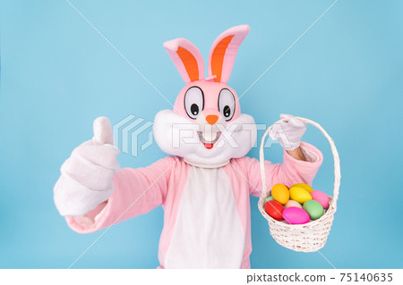 Happy easter. Easter bunny or rabbit or hare holds egg with basket of colored eggs, having fun, celebrates Easter rabbit isolated on blue background 75140635