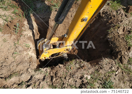 The yellow excavator digs a trench, construction works by means of automobile equipment. The yellow excavator digs a trench, construction works by means of automobile equipment. 75140722