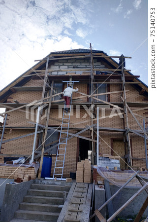 Construction and insulation of a new house with facade bricks, construction work and wooden scaffolding. Construction and insulation of a new house with facade bricks, construction work and wooden scaffolding. 75140753