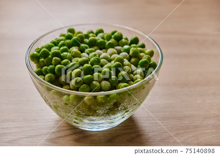 Frozen green peas in a glass plate stands on a wooden kitchen 75140898