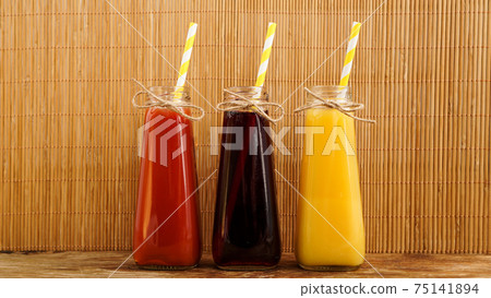 Three multicolored drinks in the bottles on a wooden bamboo background 75141894