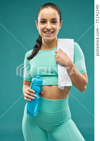 Joyful young woman in sportswear holding bottle of water Joyful young woman in sportswear holding bottle of water 75142340