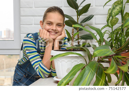 A girl examines indoor flowers and turns and looks into the frame A girl examines indoor flowers and turns and looks into the frame 75142577